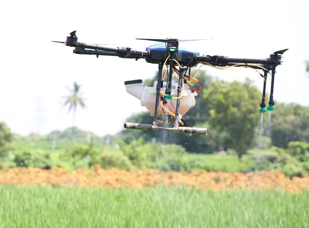 Close view of an agricultural drone spraying a fine mist above a green field